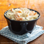 Small cup of coleslaw in a black plastic cup on top of a blue gingham napkin.