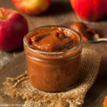 Finished apple butter in a mason jar sitting on a piece of burlap with a wood background.