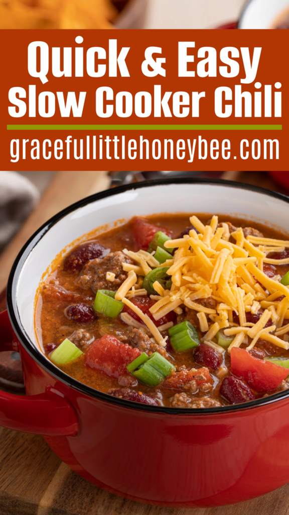 Chili in a red enamel bowl topped with cheese and green onion.