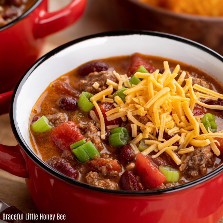 Chili in a red enamel bowl topped with cheese and green onion.