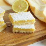 Lemon bars topped with powdered sugar on a wooden cutting board.