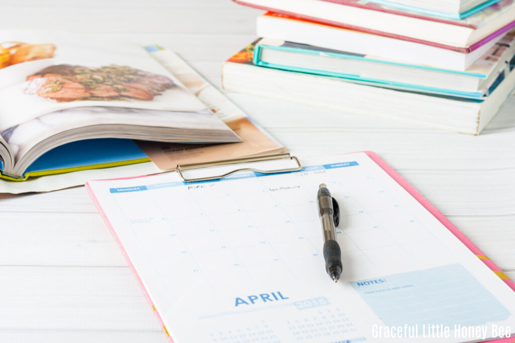 A paper meal plan sitting on a table with a black pen and cookbooks in the background.