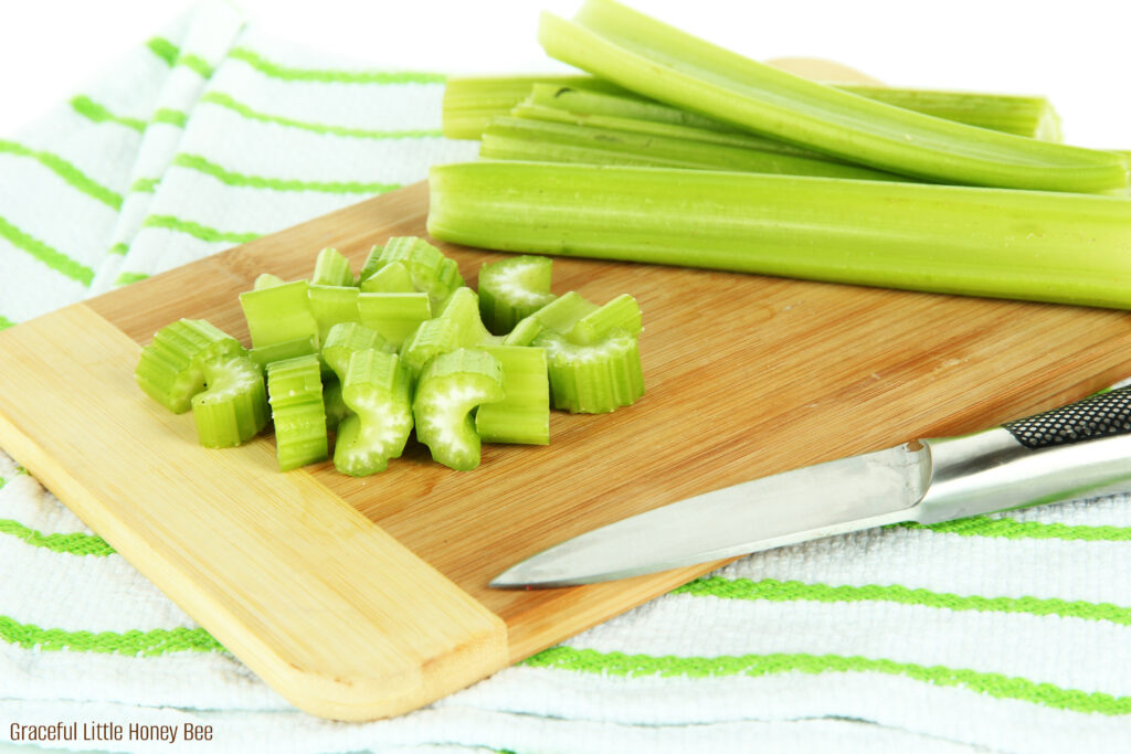 Chopped celery sitting on a cutting board with a large knife.