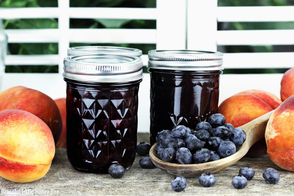 Blueberry Peach Preserves in half pint jars with fresh fruit sitting around them. 