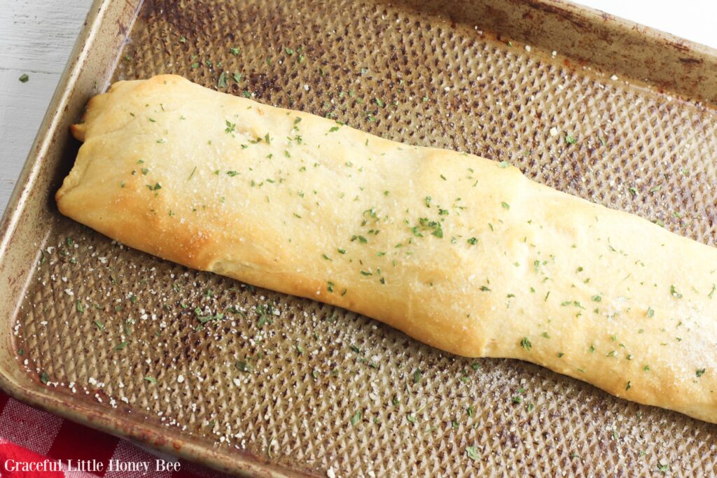 Golden brown stromboli topped with melted butter, parmesean cheese and dried parsley on a baking sheet.