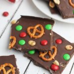 Chocolate christmas bark on a baking sheet with pretzels, peanuts and candies.