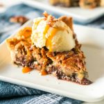 A slice of Kentucky Derby Day pie on a white plate with a scoop of vanilla ice cream drizzled with caramal and sprinkled with pecans.