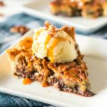 A slice of Kentucky Derby Day pie on a white plate with a scoop of vanilla ice cream drizzled with caramal and sprinkled with pecans.