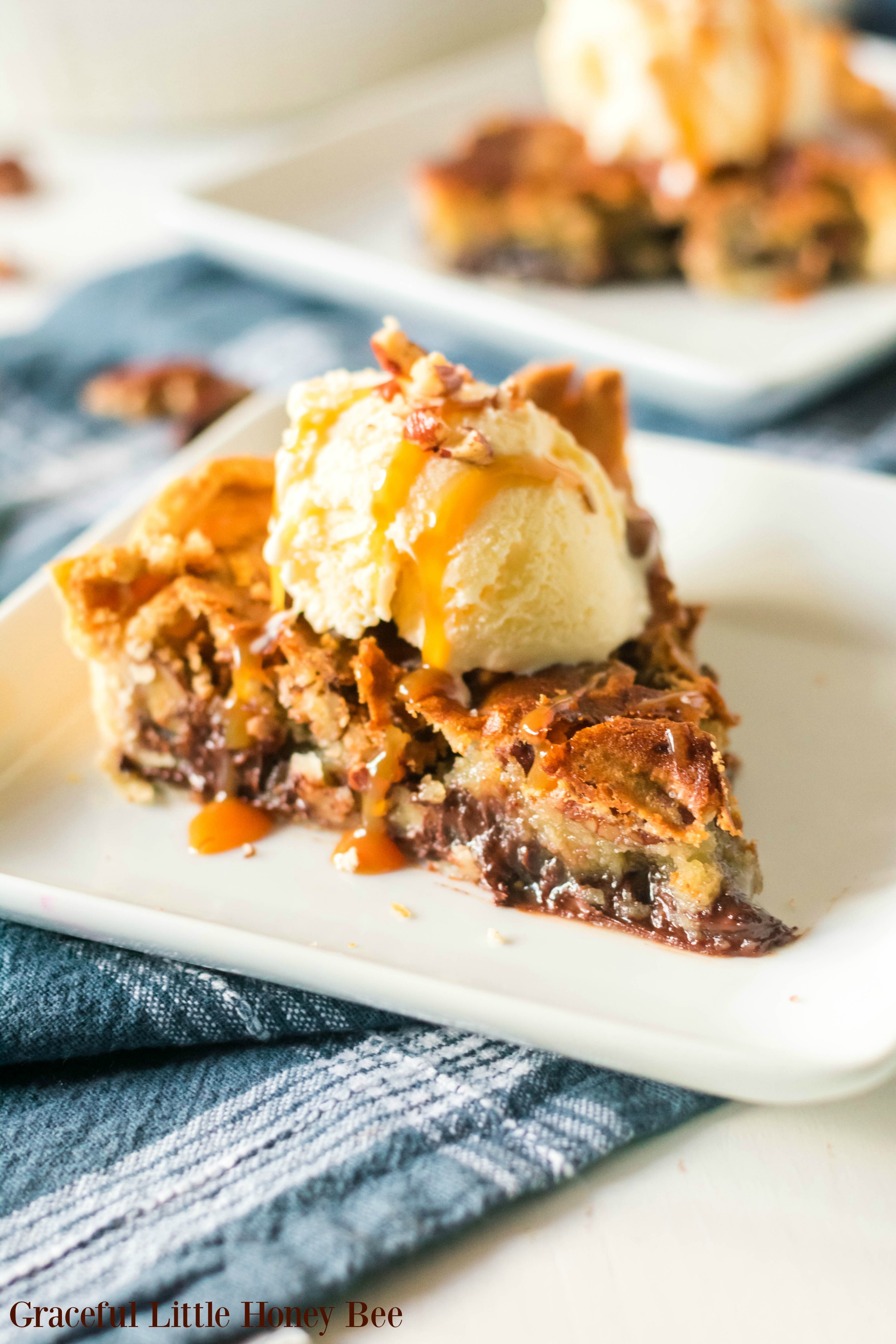 A slice of Kentucky Derby Day pie on a white plate with a scoop of vanilla ice cream drizzled with caramal and sprinkled with pecans.