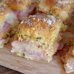 Ham and cheese sliders sitting on a wooden cutting board.