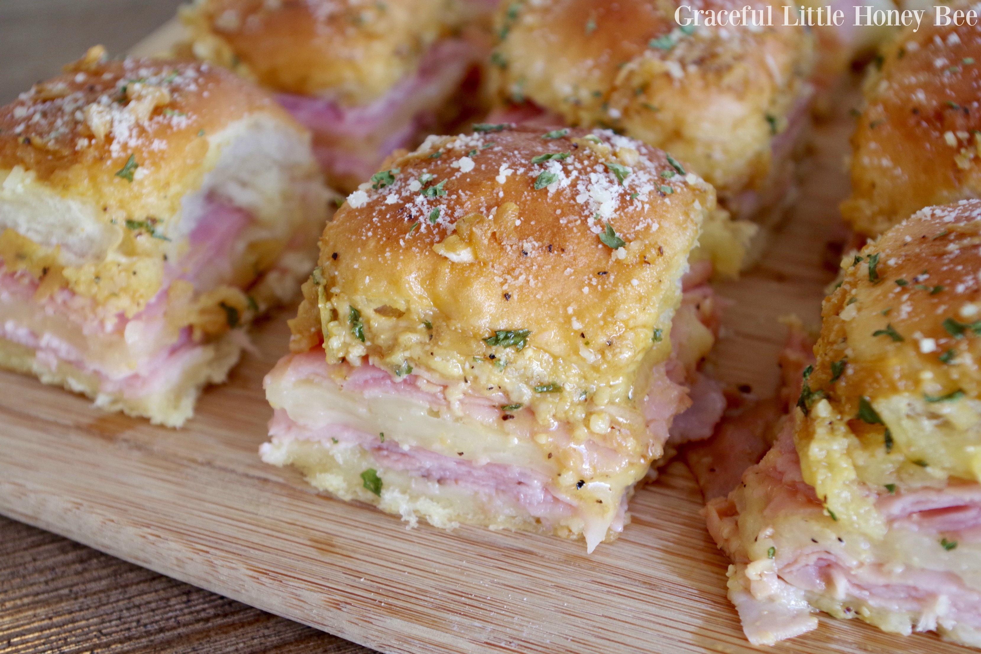 Ham and cheese sliders sitting on a wooden cutting board.