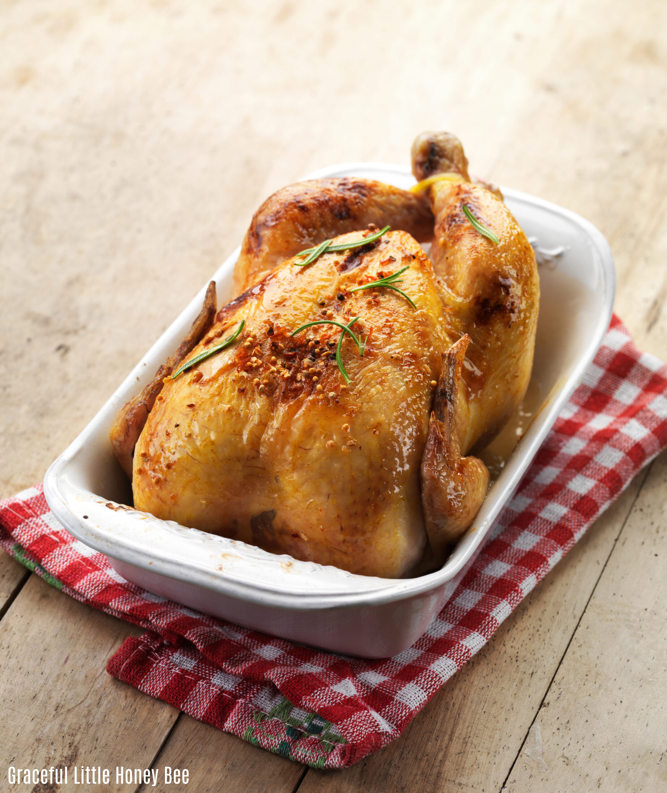 Roast chicken in a white baking dish sitting on a red and white checkered dishcloth.