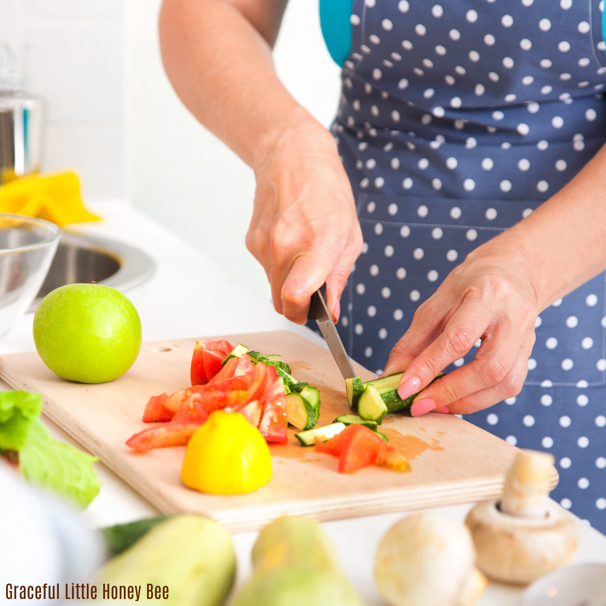 Woman slicing vegetables while wearing a blue apron with white polka dots.