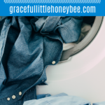 A laundry basket outside of a dryer with blue shirts hanging out.
