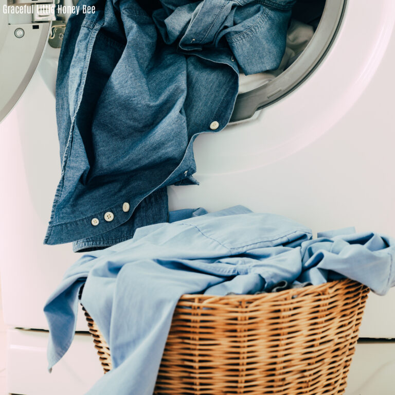 A laundry basket outside of a dryer with blue shirts hanging out.