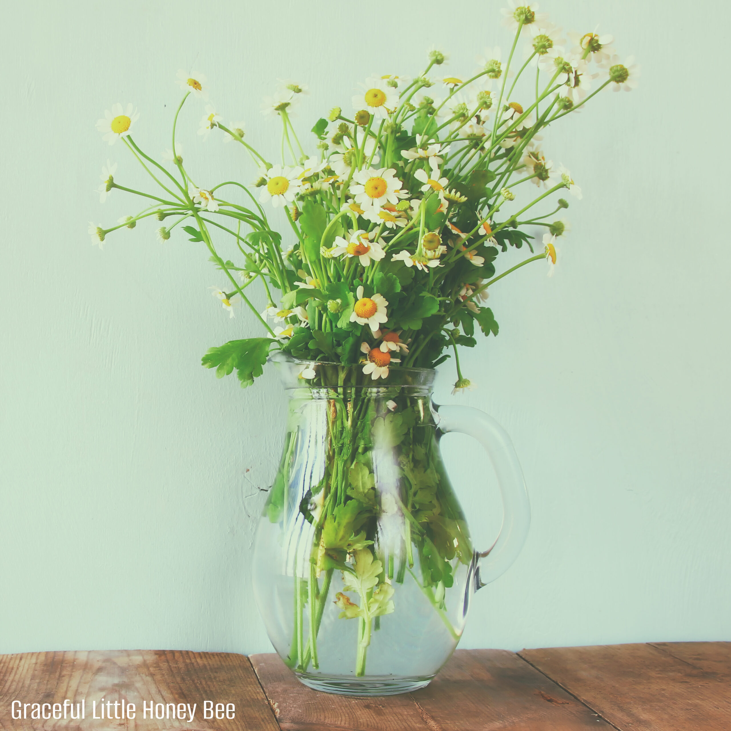 Wildflowers in glass vase sitting on a wooden table with green walls behind it.