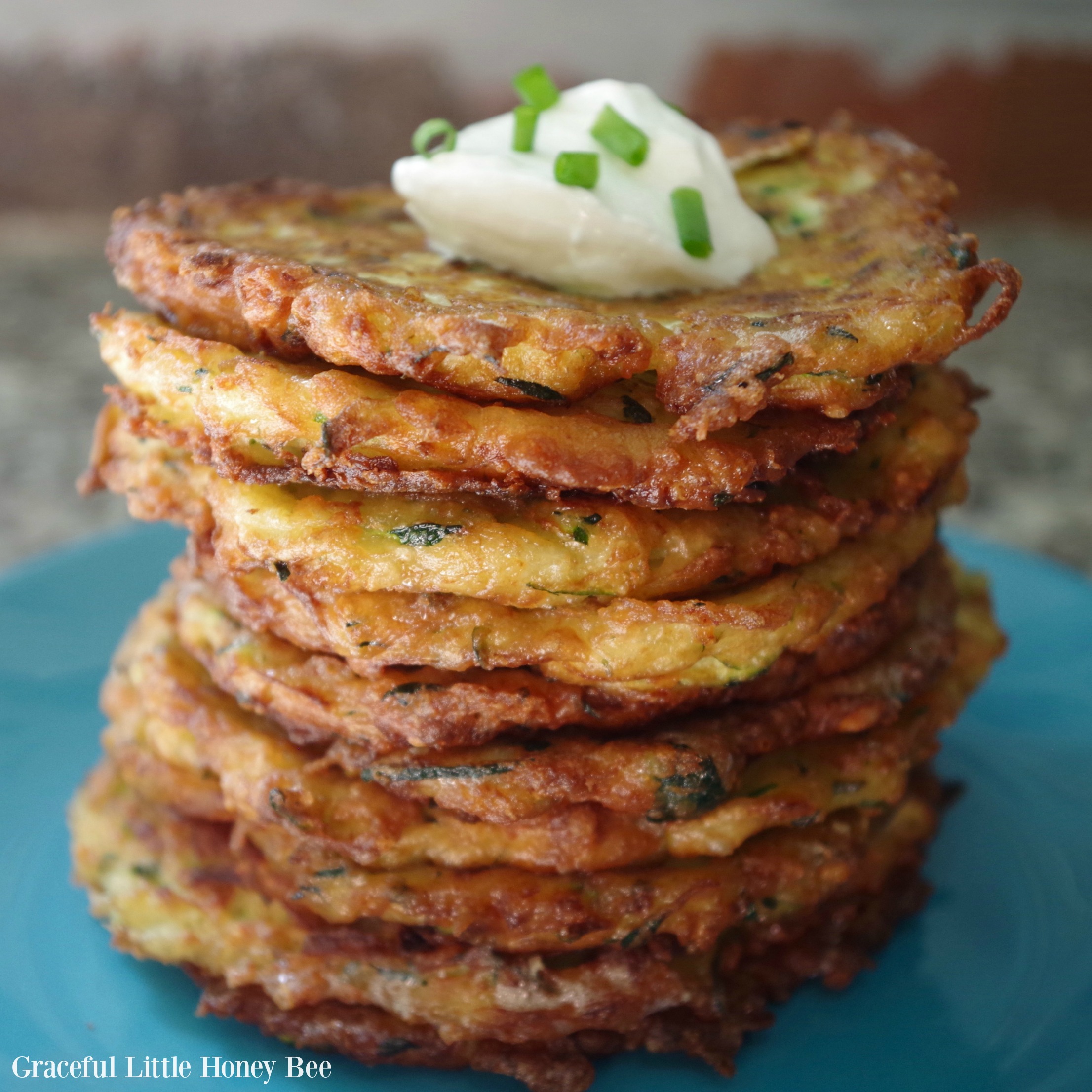 Finished fritters stacked on blue plate with a dollop of sour cream and green onions sprinkled on top.