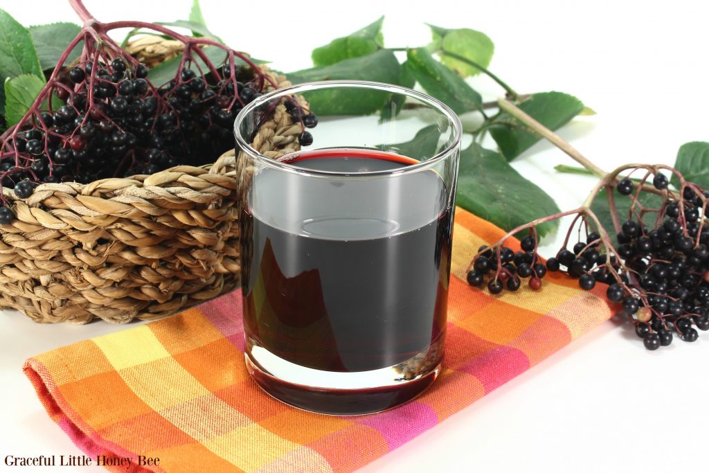 Elderberry juice with elder berries and leaves on a white background.