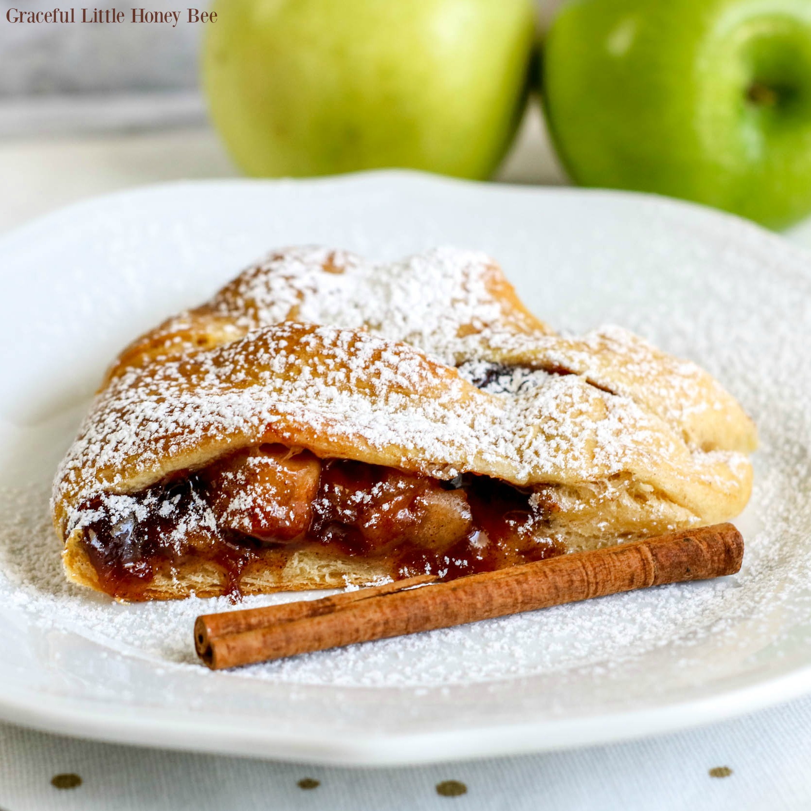 A slice of the apple pie crescent roll ring on a white plate sprinkled with powdered sugar with a cinnamon stick.