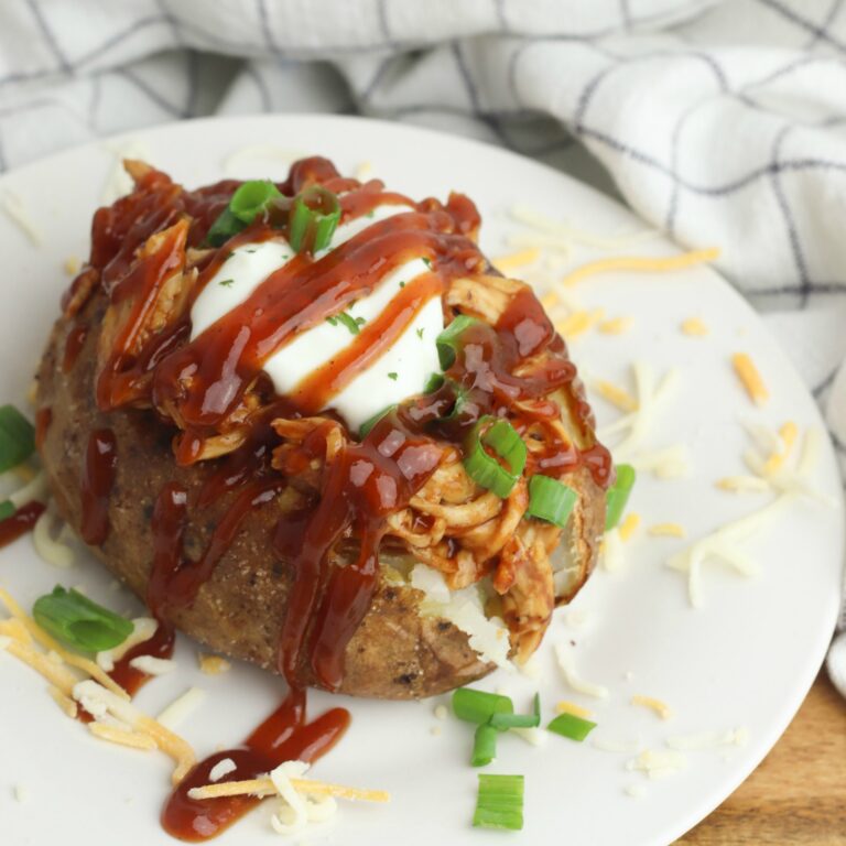 Baked potatoe with shredded BBQ turkey on a white plate.