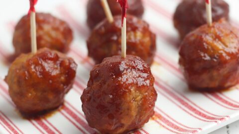Cranberry Meatballs lined up on a red and white striped plate with party toothpicks in them.