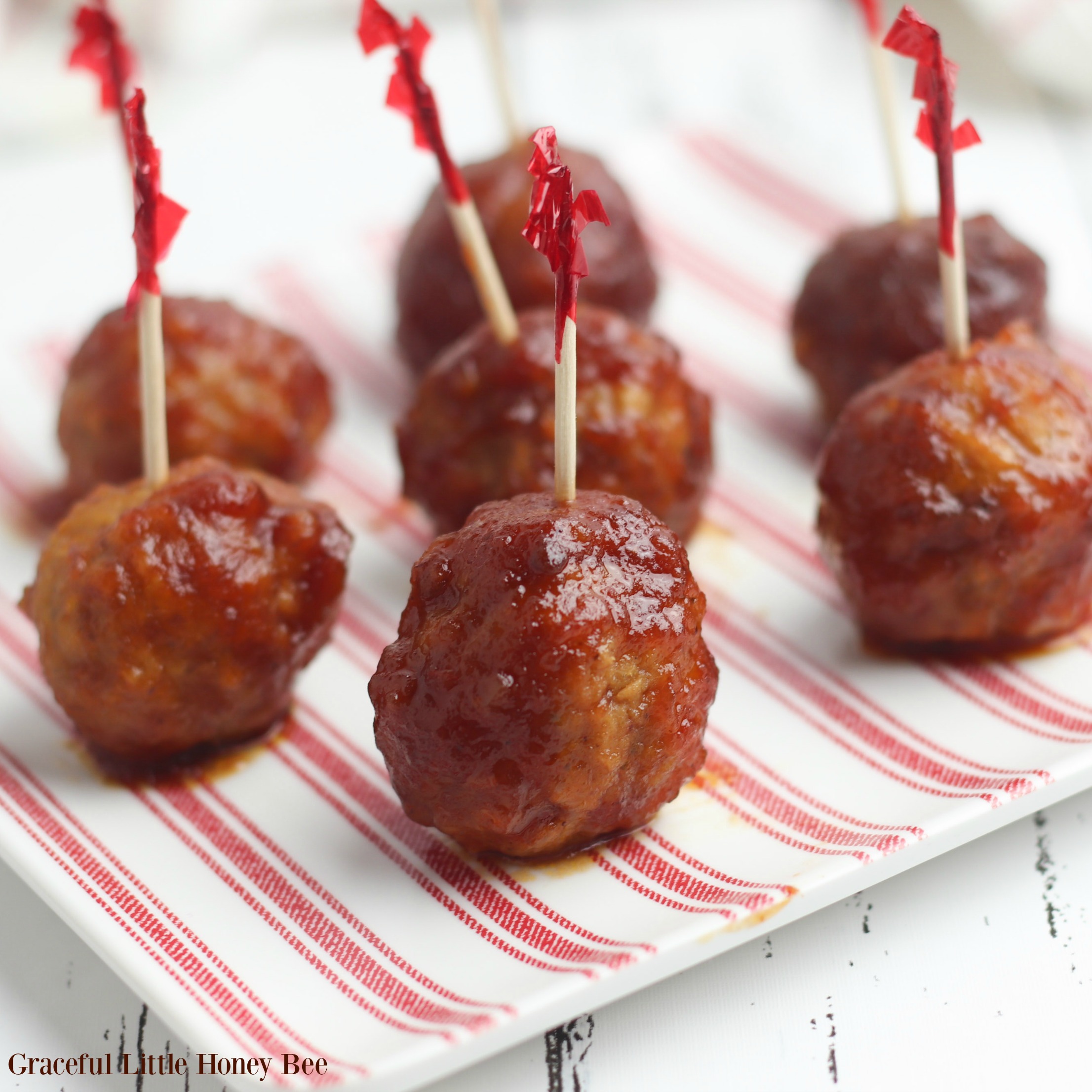 Cranberry Meatballs lined up on a red and white striped plate with party toothpicks in them.