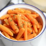 Cooked baby carrots on a white bowl.