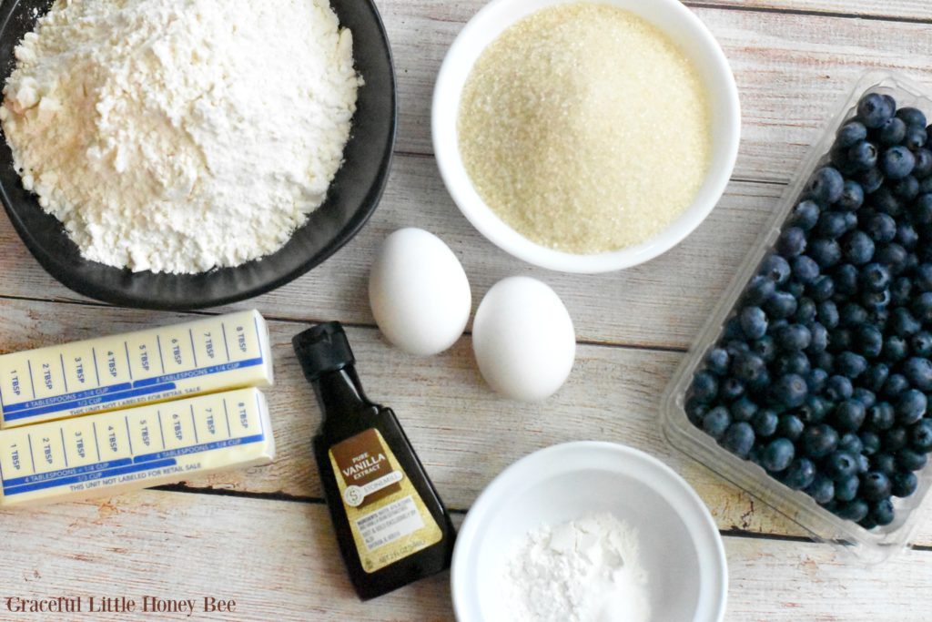 Ingredients for blueberry bread laid out on a whitewashed wooden board.