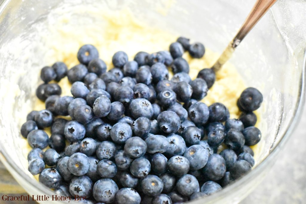 Blueberries in a bowl with bread dough and a wooden spoon.