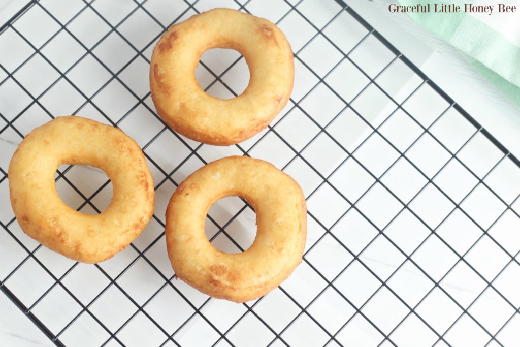 Three fried biscuit donuts on a cooling rack.