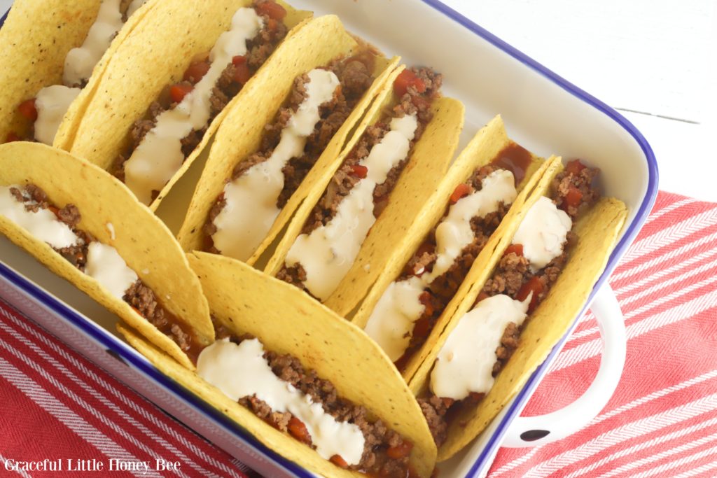 Taco shells filled with ground beef, refried beans and queso dip ready for the oven.