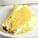 Two beef tacos topped with lettuce sitting on a white plate.
