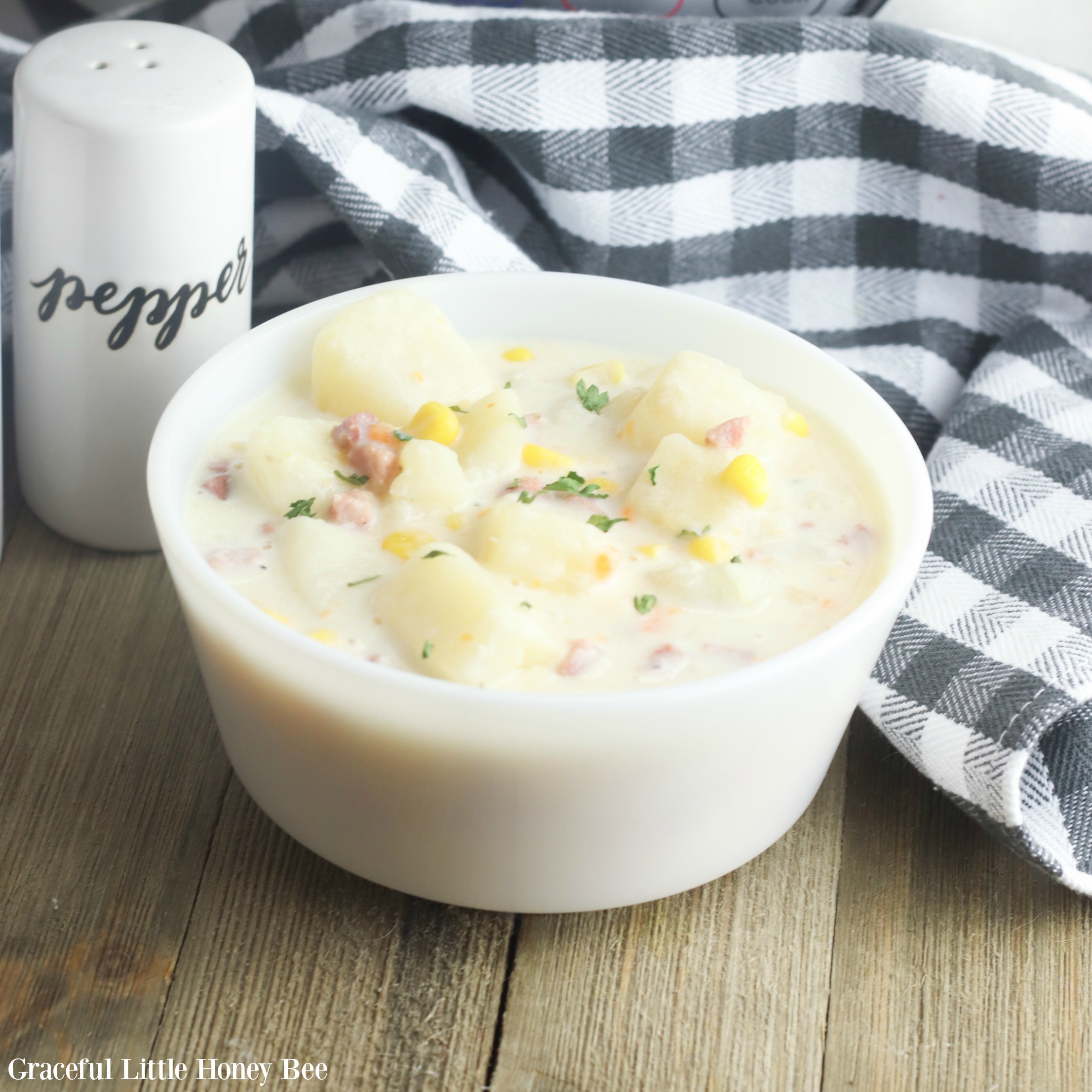 Finished chowder in a white bowl sitting on a blue buffalo check towel.