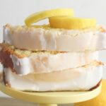 Finished pound cake slices sitting on a cake stand with lemon slices laying on top.