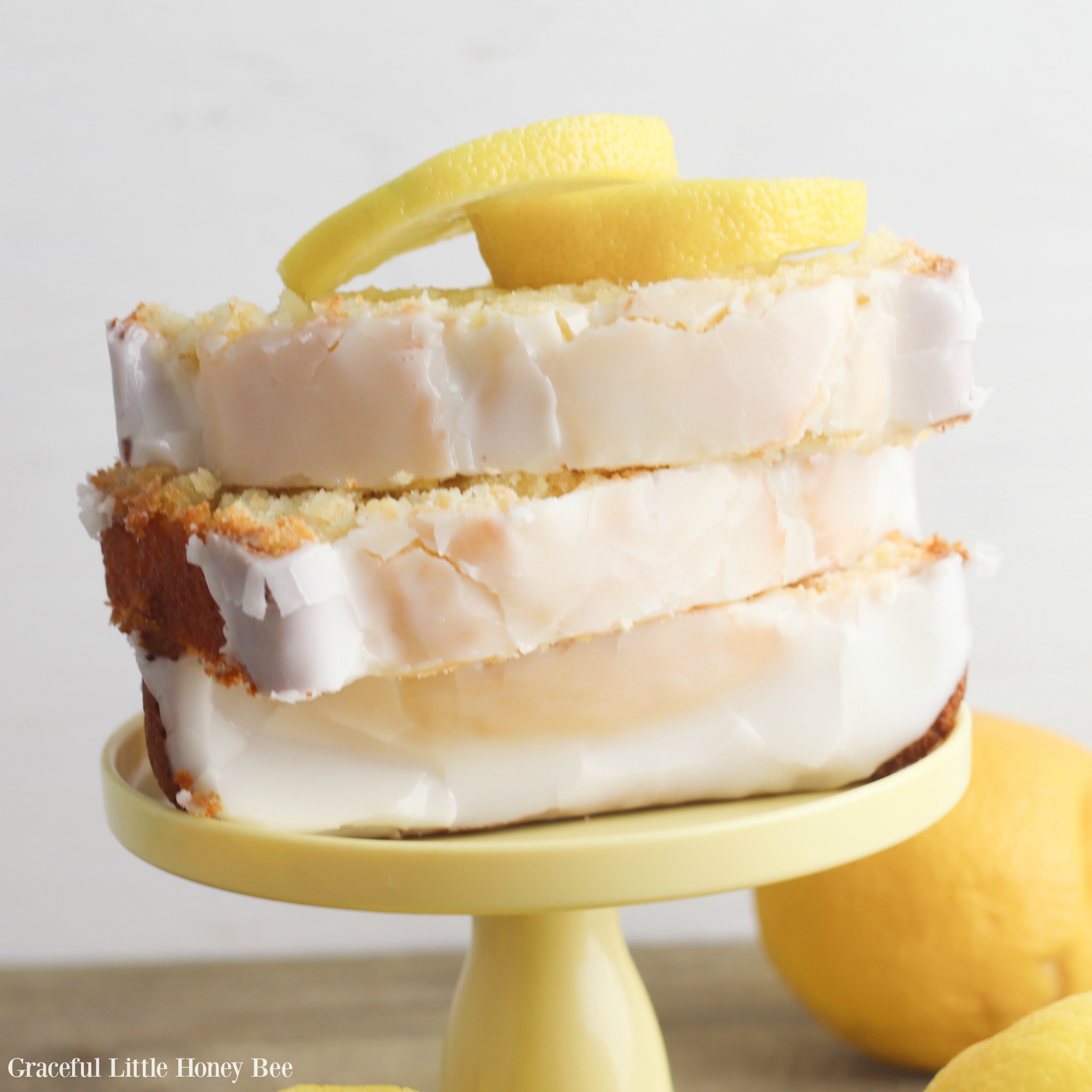 Finished pound cake slices sitting on a cake stand with lemon slices laying on top.