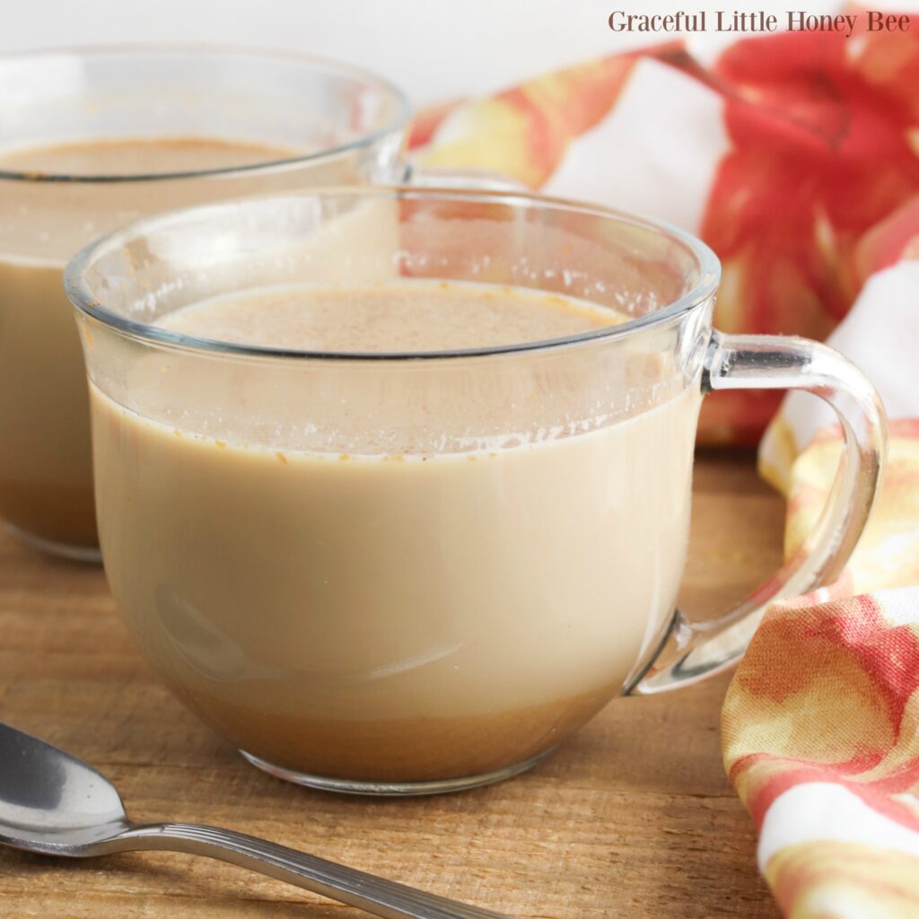 Pumpkin Spice Latte in a clear glass coffee cup sitting on a wooden board.