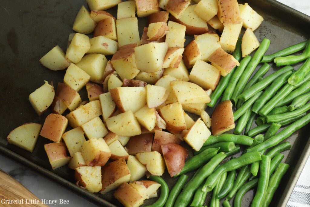 Fresh green beans and raw potaotes lined up on a baking sheet.