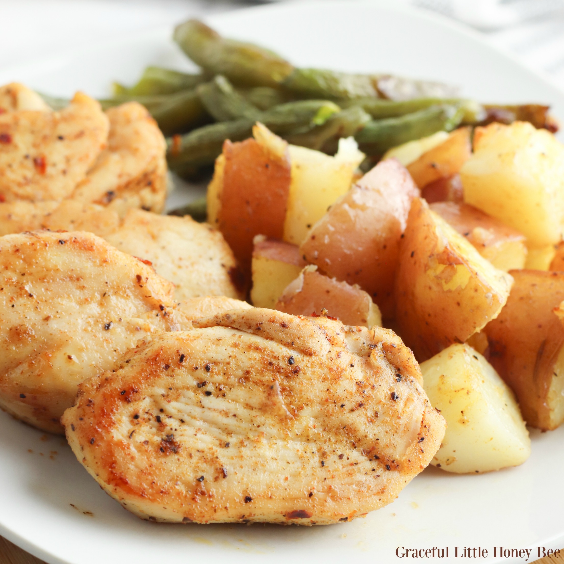 Cooked Cajun chicken, green beans and roasted potatoes on a white dinner plate.