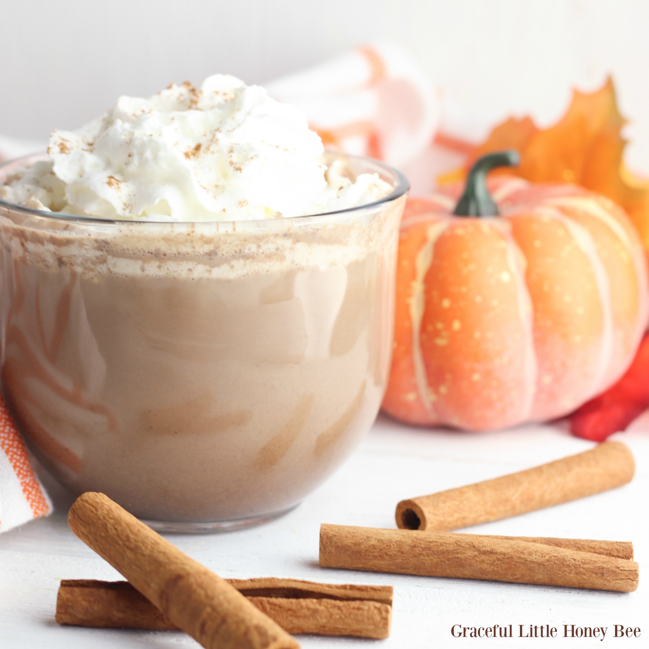 Pumpkin Hot Chocolate in a glass mug with whipped cream and cinnamon sticks.