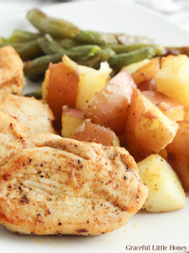 Cooked Cajun chicken, green beans and roasted potatoes on a white dinner plate.