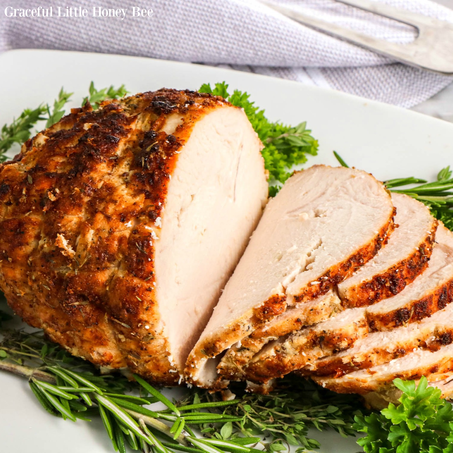 Air Fryer Turkey Breast, sliced on a white platter surrounded by fresh herbs.