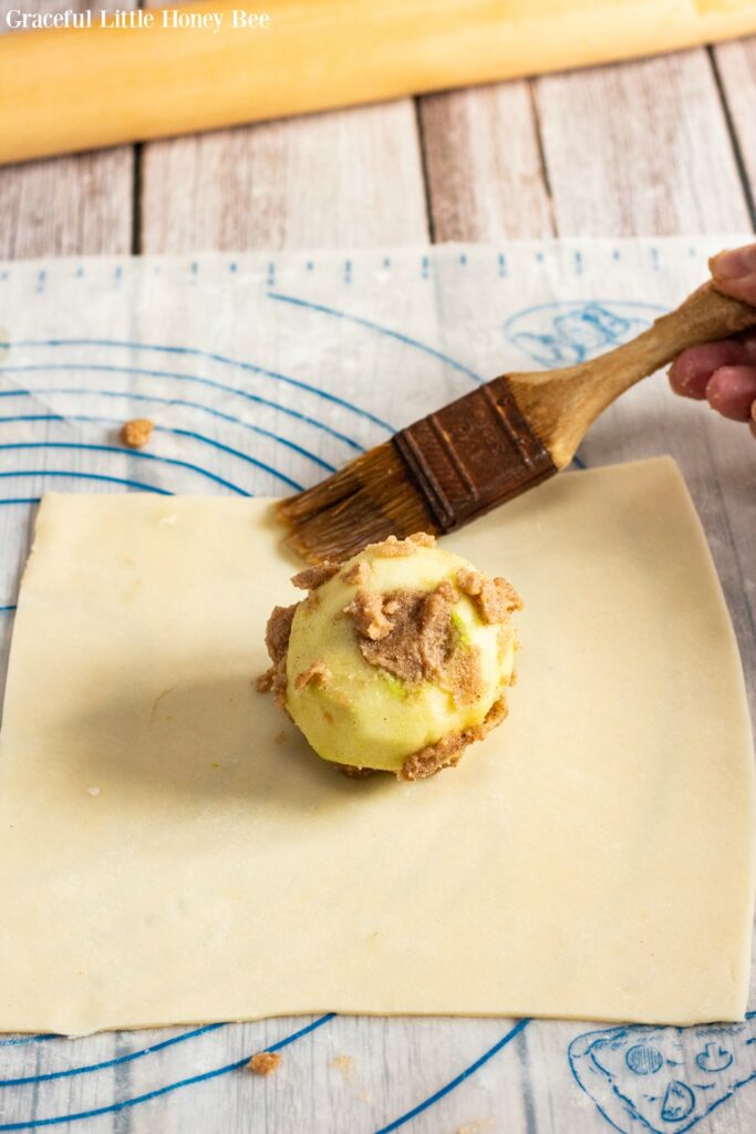 Pie crust laid flat with cinnamon sugar apple in the middle ready to be wrapped.