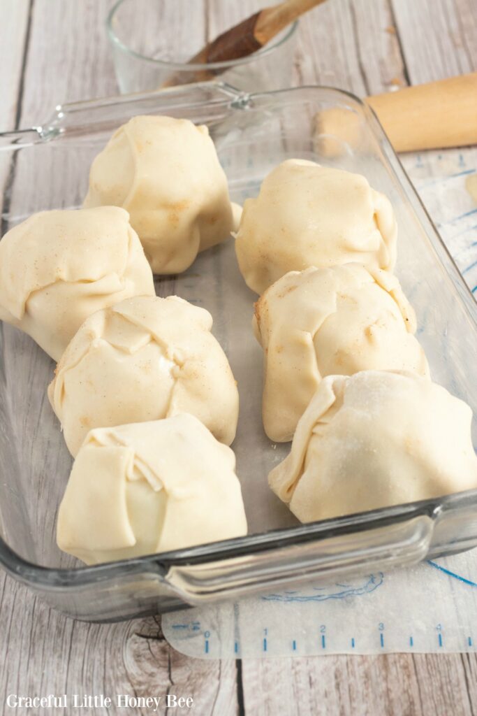 Seven apples wrapped in pie dough in a baking dish ready to go into the oven.