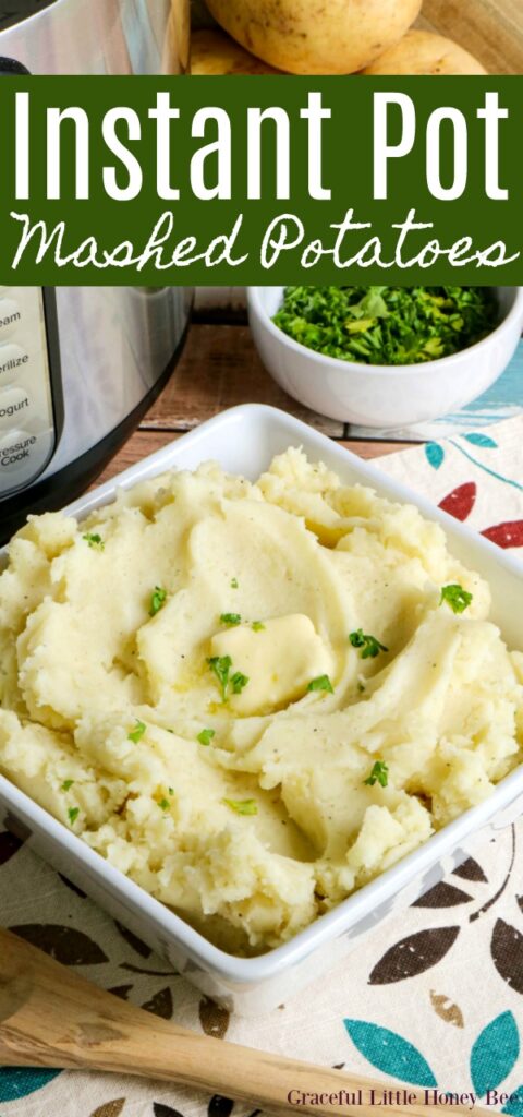 Fluffy, golden mashed potatoes in a white serving bowl with butter and parsley sprinkled on top. Potatoes, chopped parsley, a serving spoon and the Instant Pot are in the background.