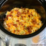 Finished Cream Cheese Chicken topped with cheese, bacon and green onions in black crock-pot.