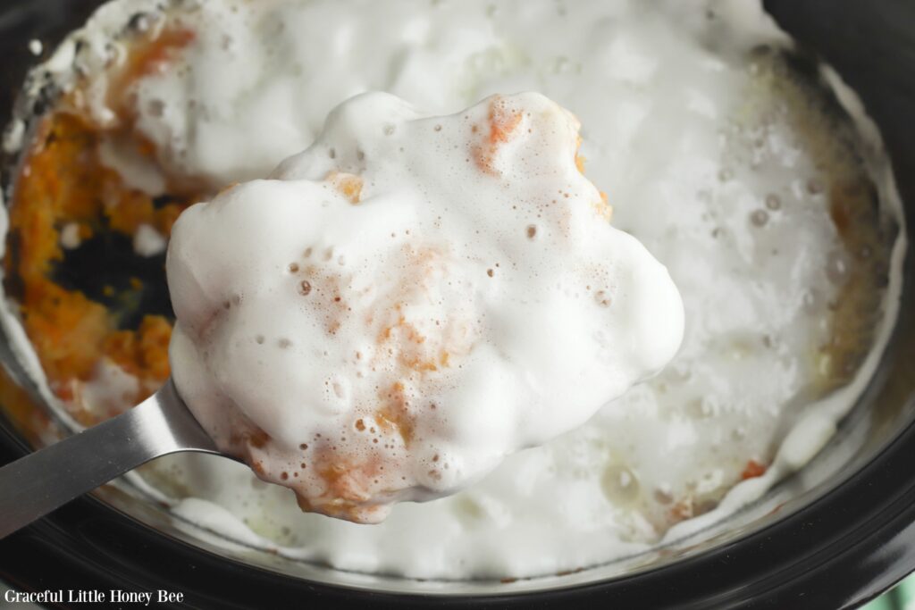 Cooked Sweet Potato Casserole with melted marshmallows on top in black slow cooker.