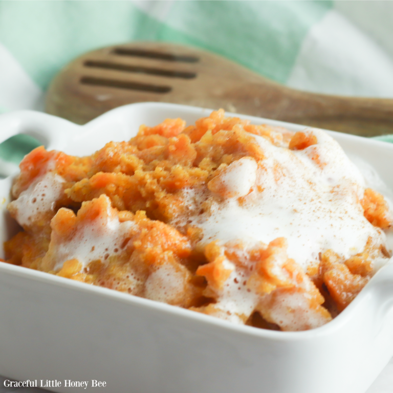 Sweet Potato Casserole with melted marshmallows on top in a white serving dish with a wooden spoon and dishtowel in the background.