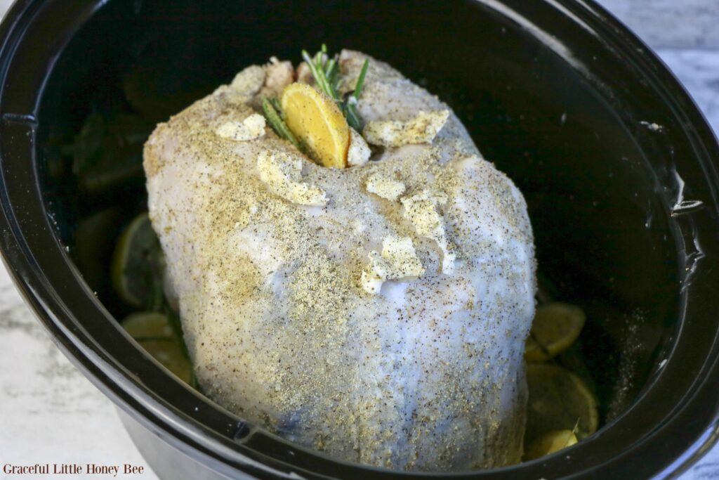 Uncooked turkey breast with lemon and rosemary on top in slow cooker.
