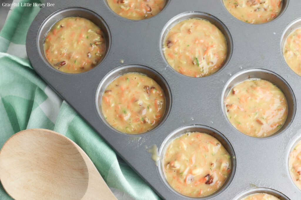 Muffin batter in muffin tin laying on a mint green towel with a wooden spoon next to the pan.