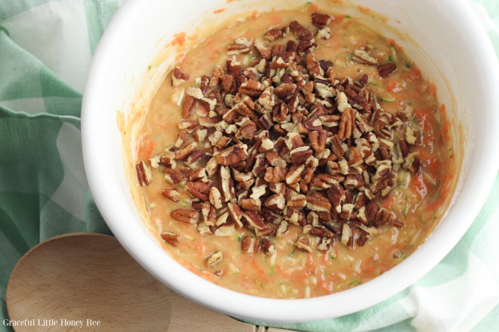 Muffin batter in a white bowl, with chopped pecans sprinkled on the top.